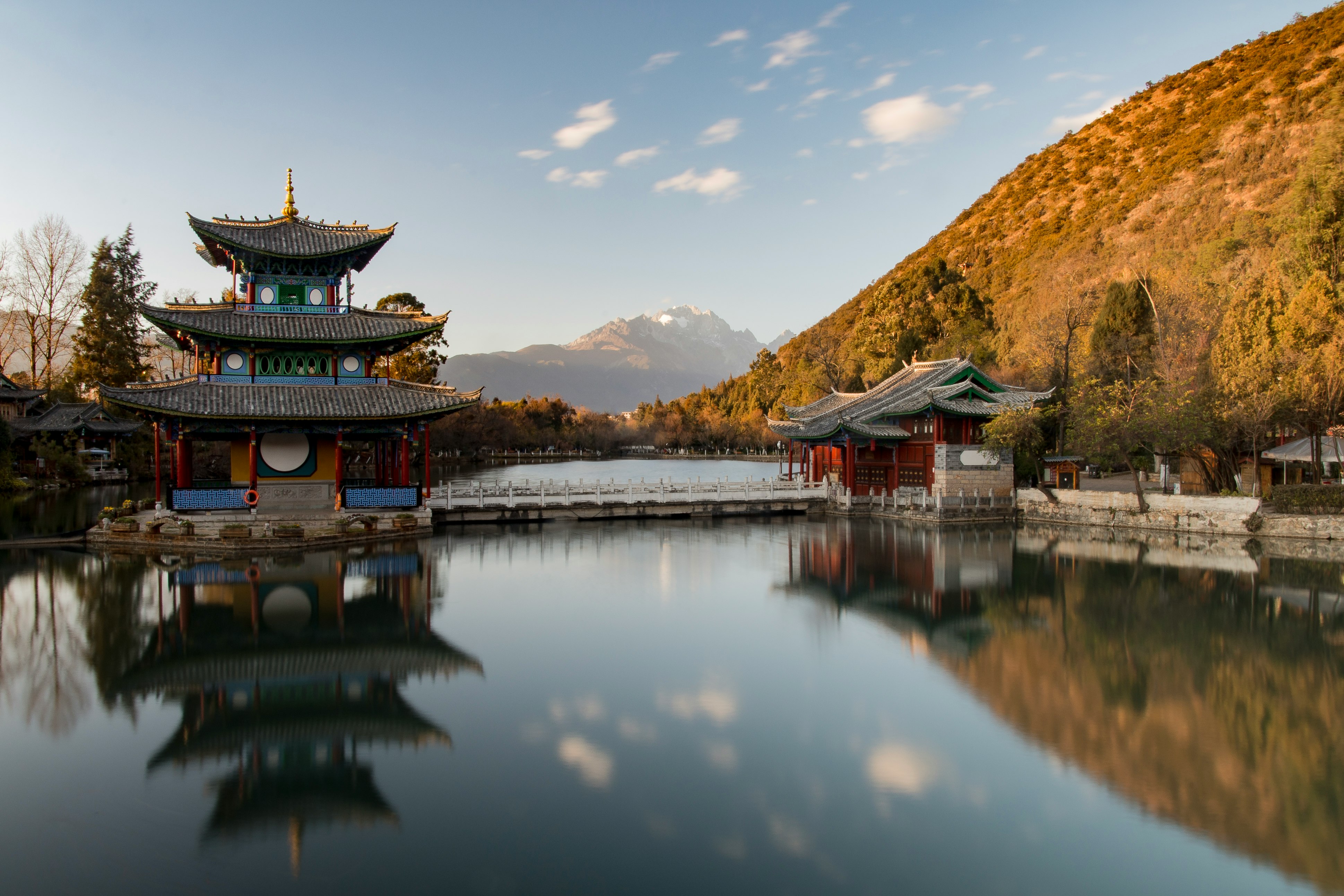 brown and green pagoda on body of water near mountain under blue sky during daytime